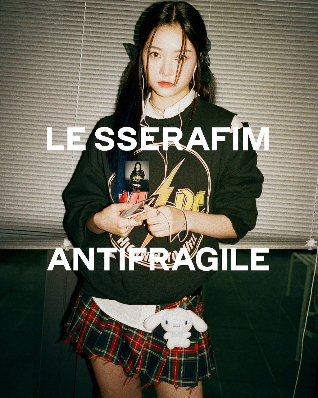 Young woman in graphic sweatshirt and plaid skirt with LE SSERAFIM Antifragile text overlay