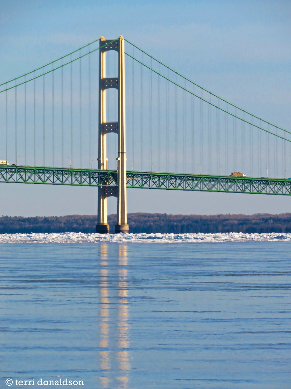 Suspension bridge tower over calm blue water with ice near the far shore
