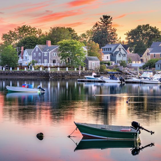 Peaceful harbor scene at sunset with boats and waterfront homes reflected in calm water