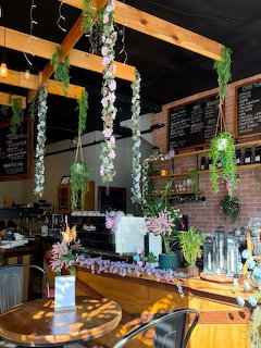 Coffee shop interior with hanging plants, wooden beams, brick walls, and natural sunlight