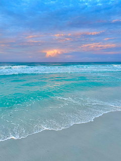 Turquoise ocean waves on white sand beach with pastel sunset sky and colorful clouds