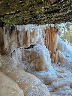 Large ice formations and icicles beneath a rocky cliff overhang in winter