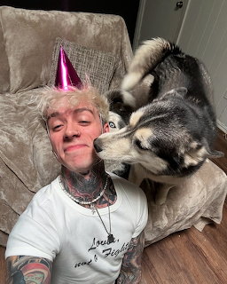 Tattooed man in pink party hat on couch with Siberian Husky dog