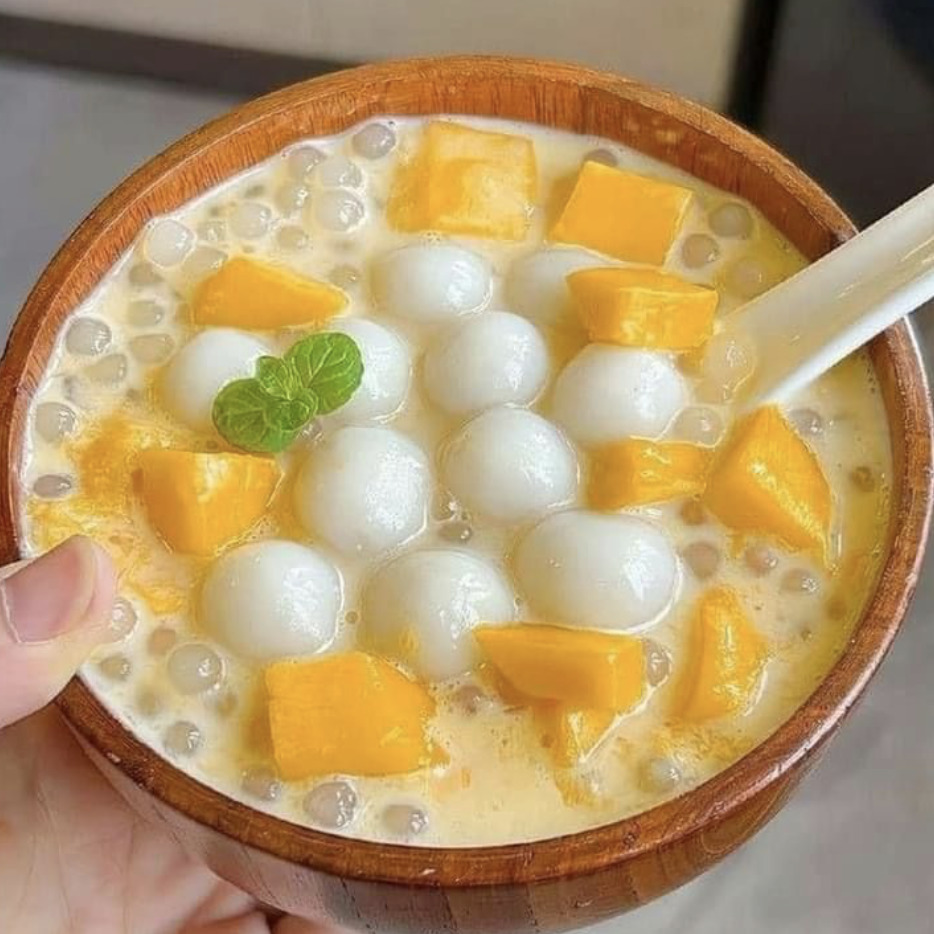 Bowl of mango sago dessert with tapioca pearls, fresh mango pieces, and coconut milk topped with mint leaf