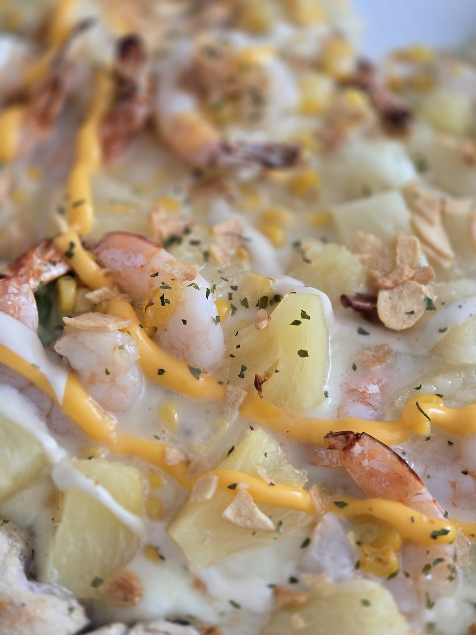Close-up of Korean shrimp pizza with pineapple, shrimp, melted cheese and yellow sauce drizzle