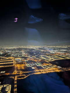 Aerial night view of a city grid lit by streetlights, seen through an airplane window
