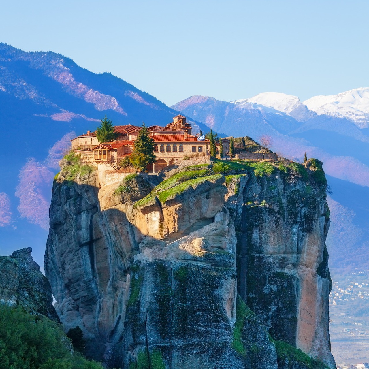 Monastery perched on a tall rock pillar with mountains behind in Meteora, Greece