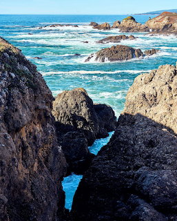 Dark volcanic rocks frame turquoise ocean waves crashing on California's Sea Ranch coast