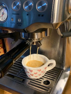 Espresso machine pouring coffee into a white mug with pink heart patterns