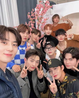 Group of nine young men posing together for a selfie indoors with pink cherry blossom decorations