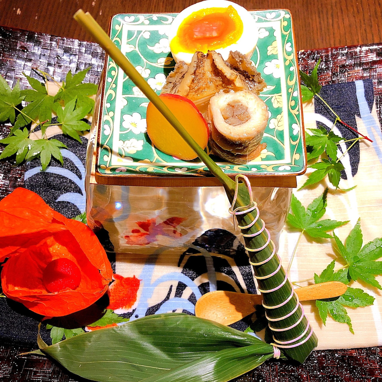 Traditional Japanese bento box with fish, egg roll, vegetables and flower garnish on decorative square plate