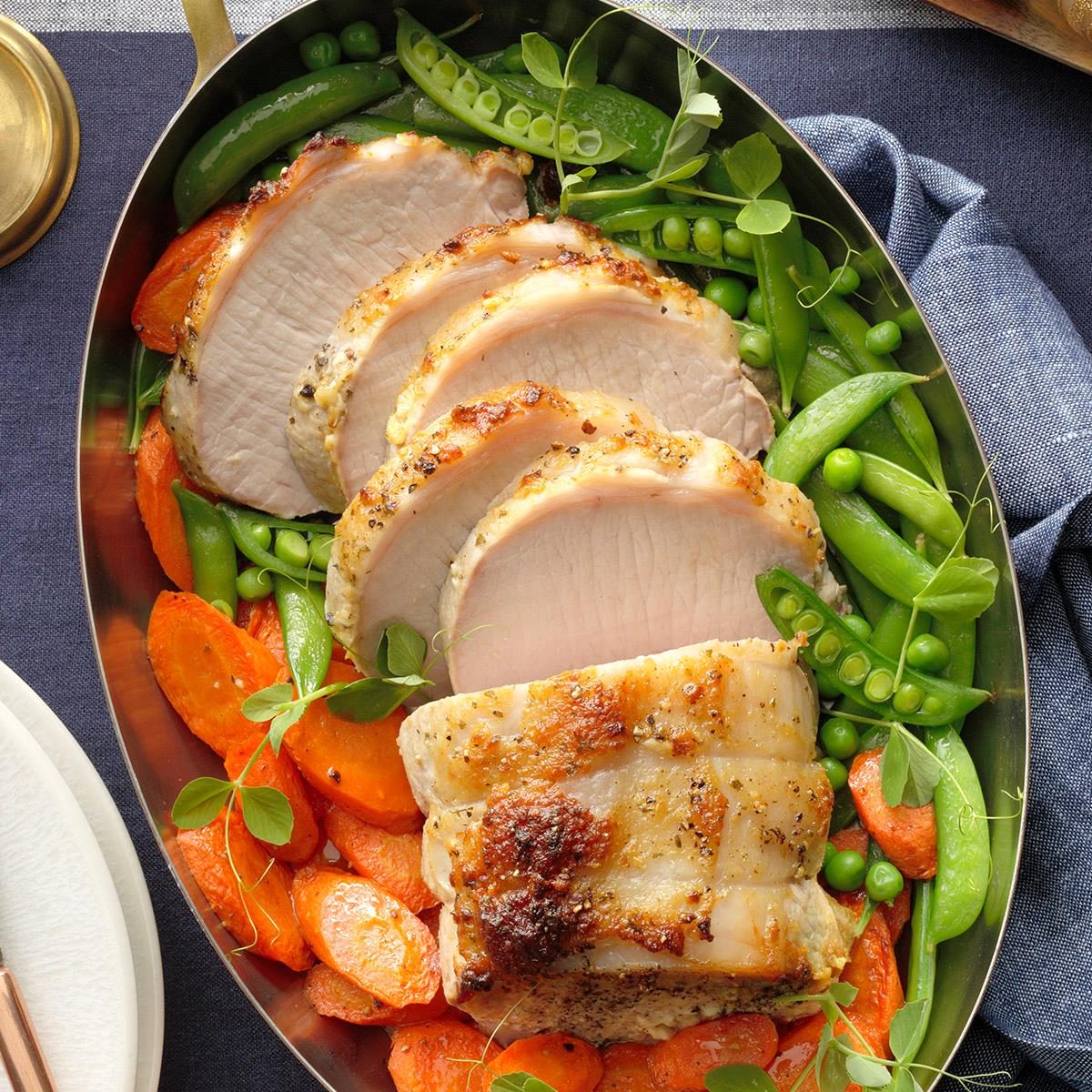 Sliced roasted pork loin on platter with carrots, snap peas, and edamame