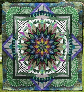 Colorful quilt pattern with a floral mandala center and geometric green fan designs