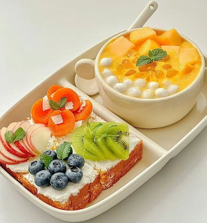 White tray with mango cream tart and colorful fruit tart garnished with fresh berries, kiwi, and mint