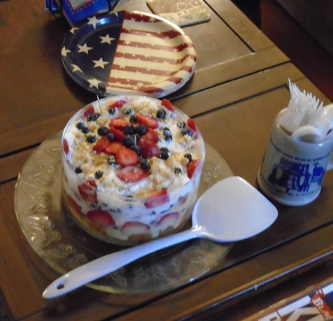 Layered trifle dessert with berries and cream, patriotic flag decoration on wooden table
