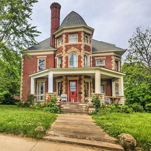 Large Victorian brick house with wraparound porch, chimney, and front walkway