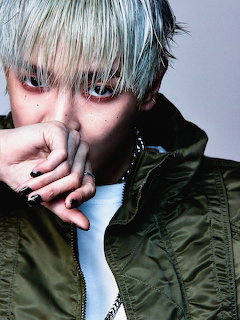 Close-up portrait of a person with blond hair, dark eye makeup, and a green jacket