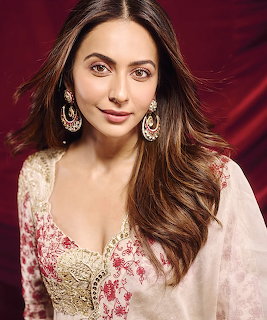 Young woman in white floral Indian attire with gold drop earrings against a red backdrop