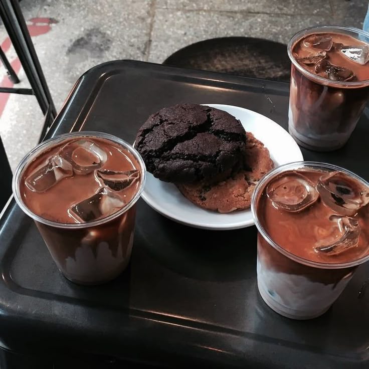 Three iced coffees on a black tray with a dark chocolate cookie on a white plate