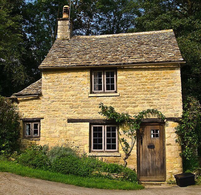 Rustic stone cottage with a tiled roof, wooden door, windows, and climbing vines