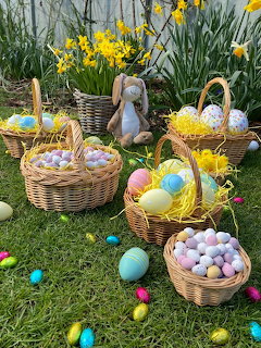 Wicker baskets filled with colorful Easter eggs on grass a plush bunny and yellow daffodils