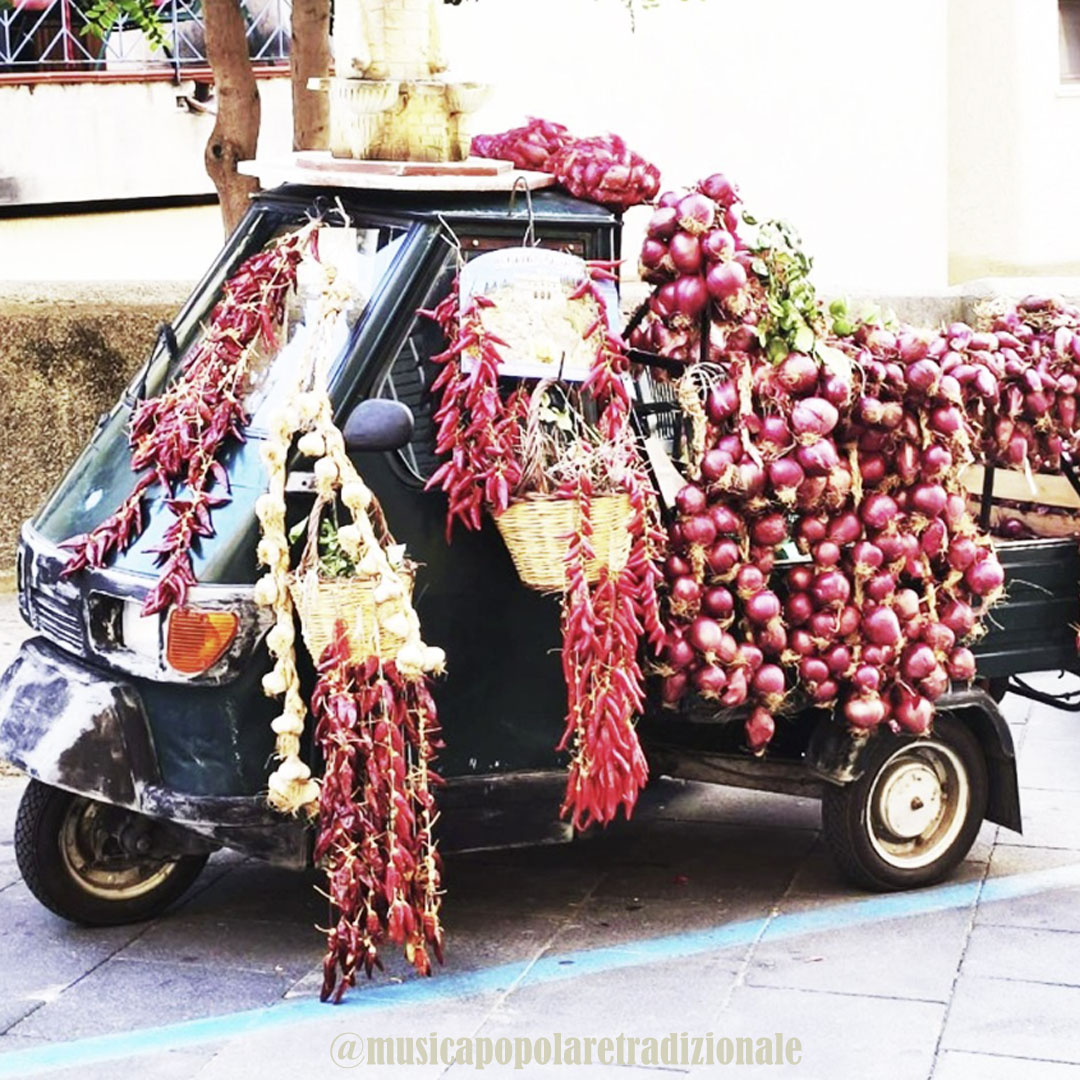 Black three-wheeler covered with red onions and hanging dried peppers on a street