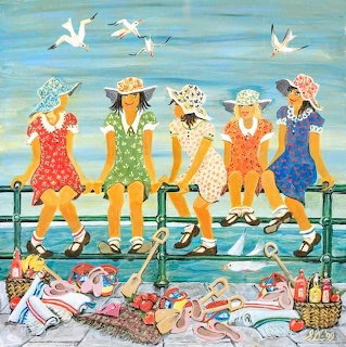 Five women in sun hats and dresses sitting on a seaside pier with beach gear and flying seagulls