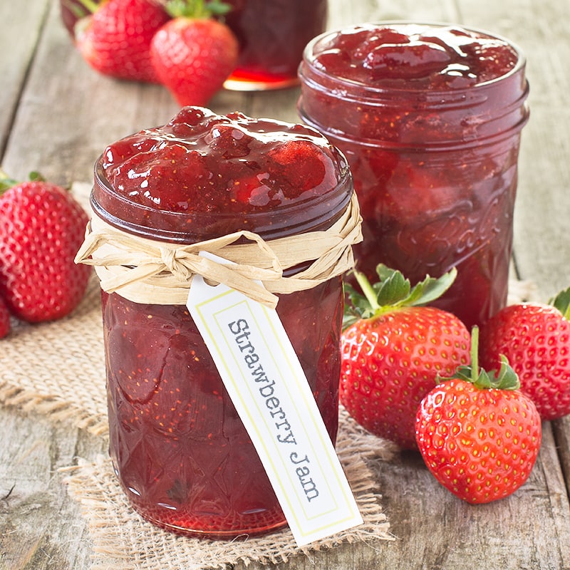 Two jars of strawberry jam with fresh strawberries on a rustic wooden table