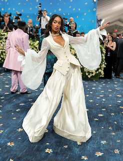 Woman in white flowing pantsuit with sheer sleeves posing on blue floral carpet at formal event