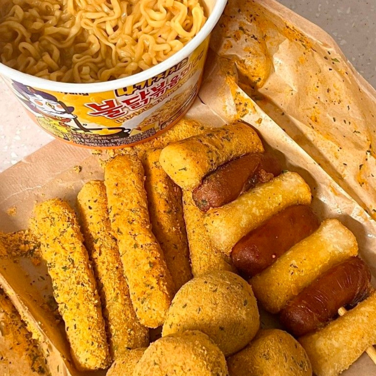Korean street food with ramen cup, fish cakes, sausages and fried chicken on brown paper