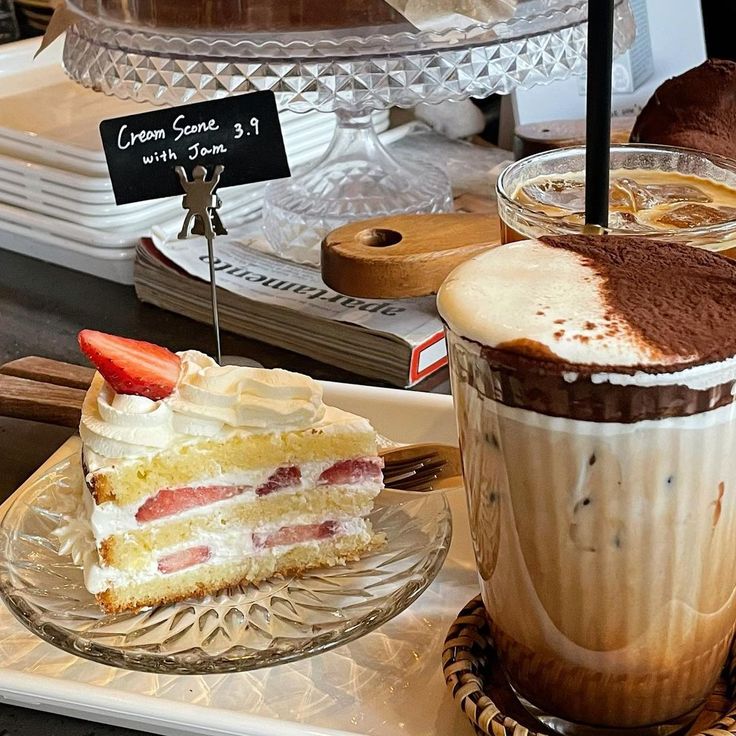 Slice of strawberry cream cake beside a tall iced coffee topped with cocoa powder