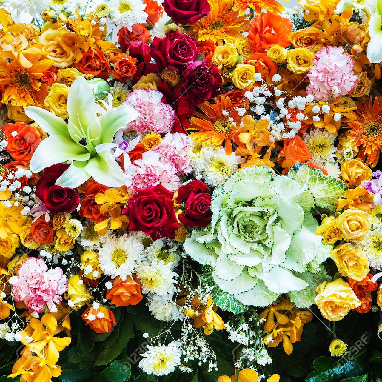 Dense arrangement of colorful roses, lilies, carnations and small daisies in warm and cool tones