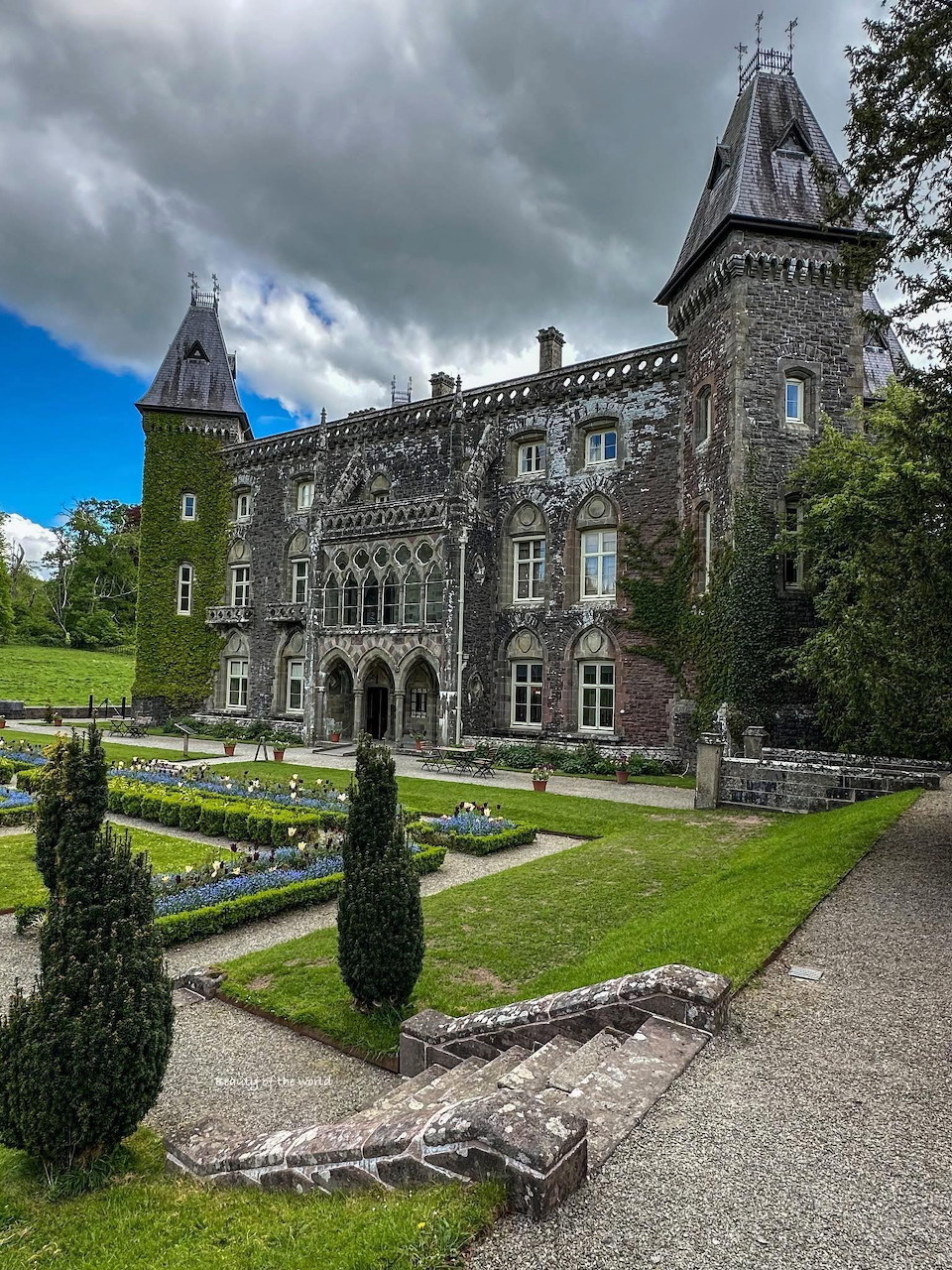 Gothic stone castle with towers and manicured gardens under a cloudy sky in Europe
