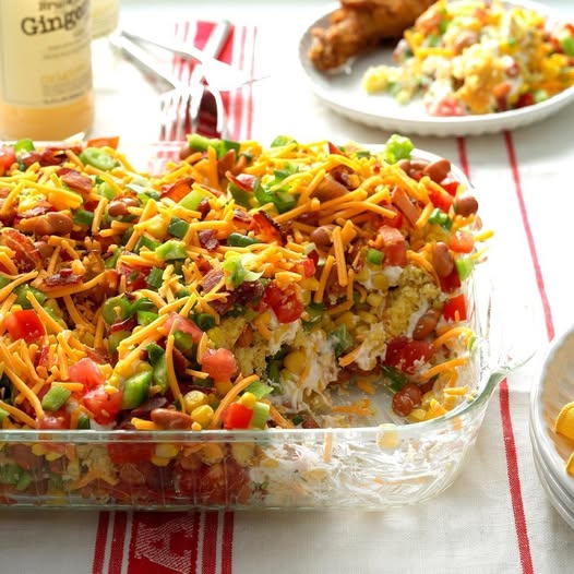 Glass baking dish of cheesy casserole with vegetables and shredded cheese on a table