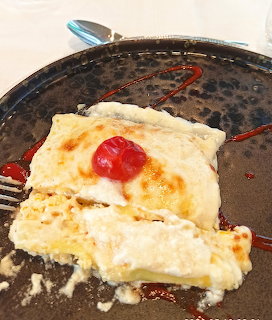 Folded crepes on a dark plate topped with a cherry and red sauce drizzle