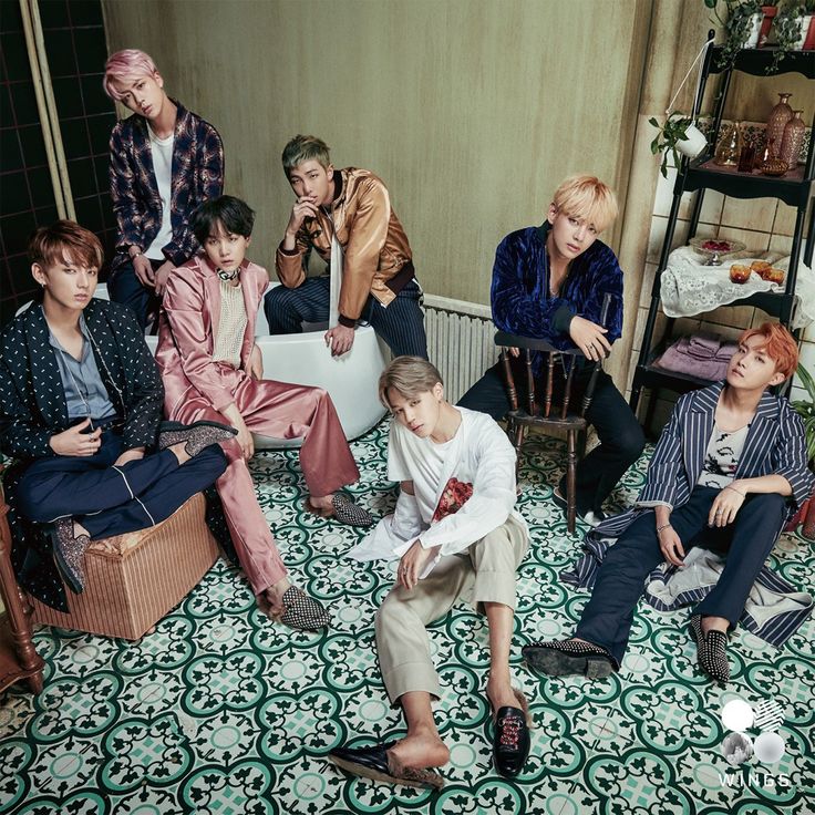 Seven young men posing in a patterned room wearing colorful fashionable outfits
