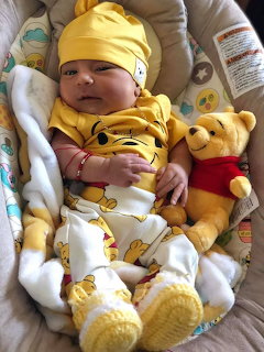 Newborn baby in yellow Winie the Pooh outfit lying in a bouncer with a Poh Bear plush toy