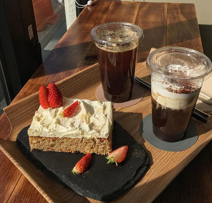 Two iced coffee beverages and strawberry cake slice with whipped cream on wooden board