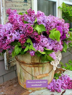 Large bouquet of purple and pink lilacs in a weathered wooden bucket on a porch