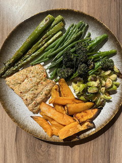 Round plate with roasted sweet potatoes, broccolini, asparagus, green beans, leks, and tempeh on wooden table