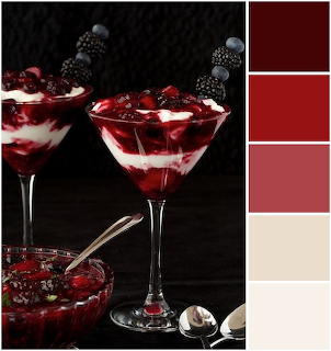 Two glasses of red berry dessert with a berry sauce bowl and a vertical color palette on a dark background.
