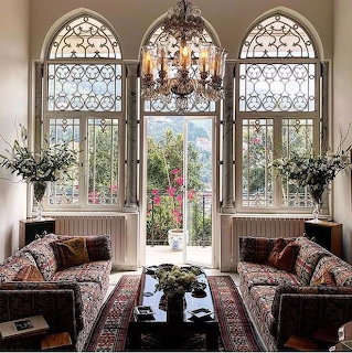 Elegant sitting room with two sofas, arched windows, chandelier, and garden view
