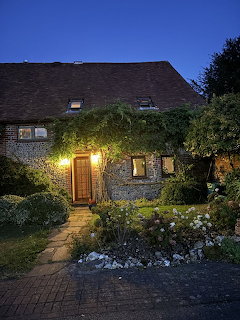 Ivy-covered cottage with lit doorway and garden at dusk