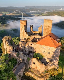 Aerial view of a medieval stone castle with towers above morning fog in a green valley