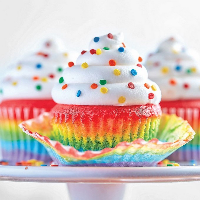 Rainbow-colored cupcakes with swirled white frosting and colorful sprinkles on a white stand