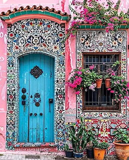 Colorful pink building with ornate blue door, decorative tile mosaics, and poted flowers