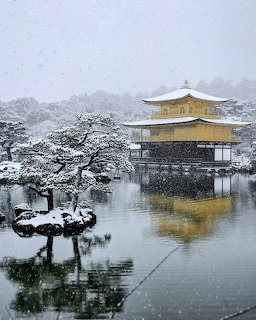 Snow-covered Kinkakuji temple reflected in a pond with winter trees