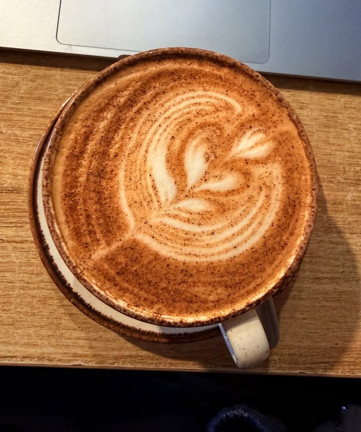 Top view of coffee with foam leaf art in ceramic cup on wooden surface
