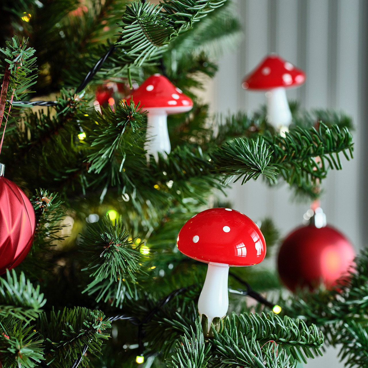 Red spotted mushroom ornaments on a Christmas tree with baubles and lights