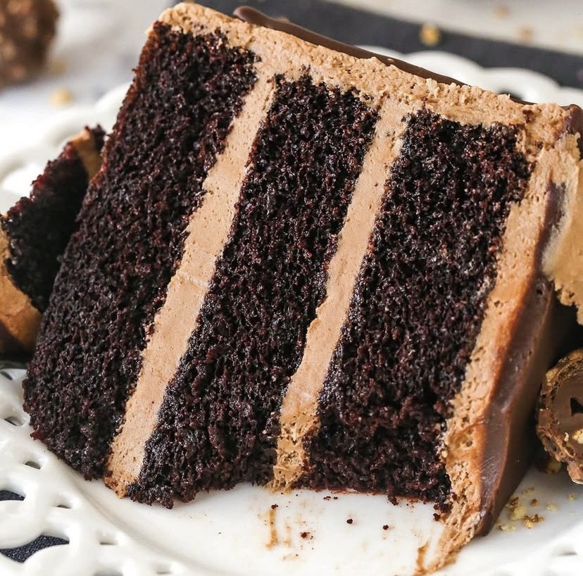 Slice of chocolate layer cake with chocolate frosting on white plate